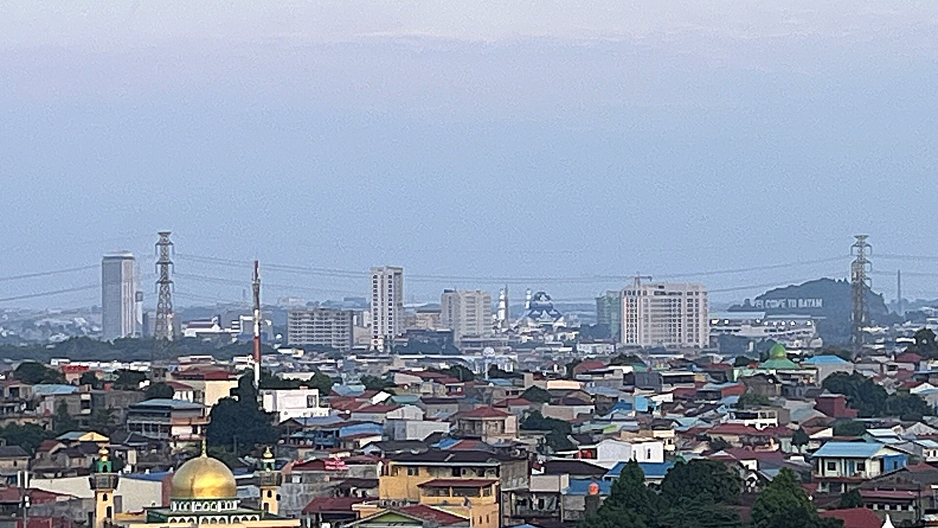 The Batam Centre skyline at dusk, with high-voltage transmission towers in the foreground